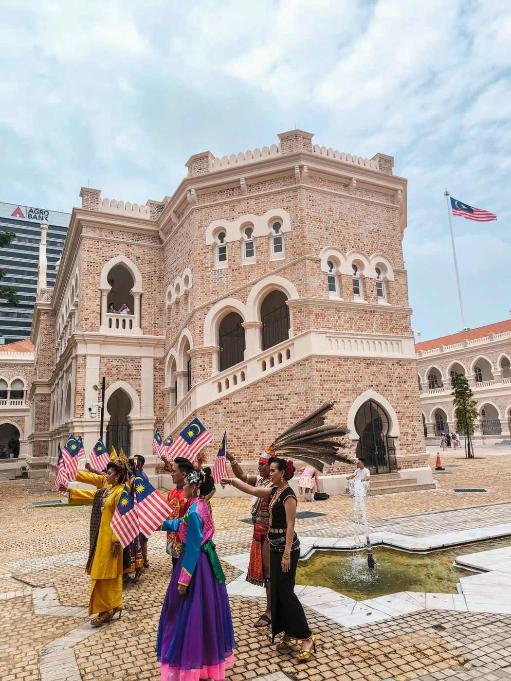 Danseurs en costumes traditionnels agitant des drapeaux malaisiens devant un bâtiment colonial de Kuala Lumpur