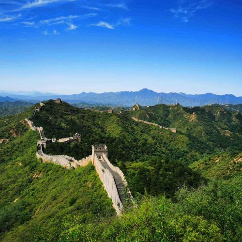 Stunning aerial view of the Great Wall of China winding over lush green hills under a clear blue sky.